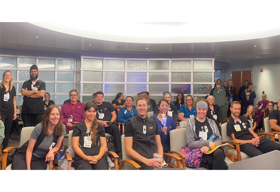 Group of people sitting and standing in rows wearing hospital scrubs.