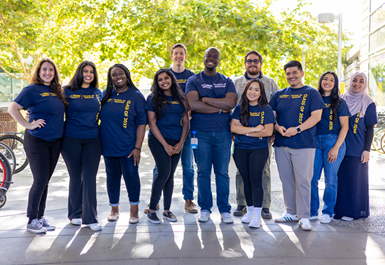 A diverse group of 12 medical students stand shoulder-to-shoulder wearing blue UC Davis t-shirts