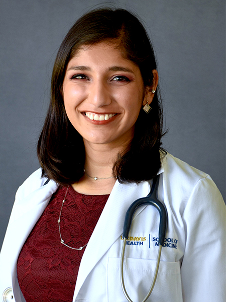 A young woman with dark hair past her shoulders, red wine-colored top and white lab coat, and stethoscope around her neck