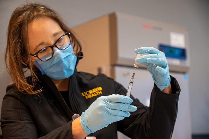 Nurse wearing a blue mask is filling a needle with vaccine.