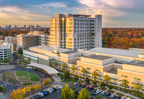 Aerial view of UC Davis Medical Center lit gold by the sun setting to the left side of the building.