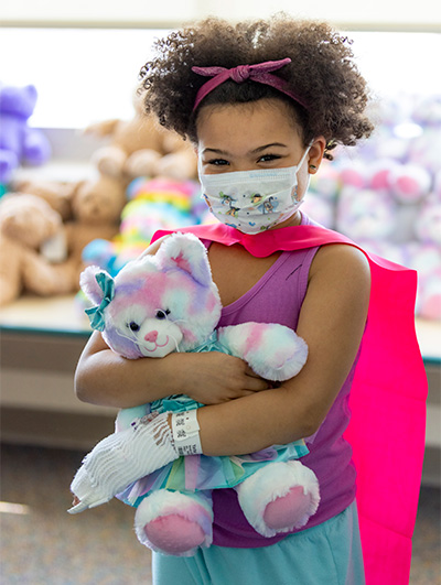 Child with mask hugging stuffed teddy bear 