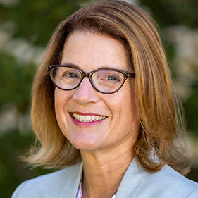 A woman wearing a light blue suit stands in front of the UC Davis MIND Institute