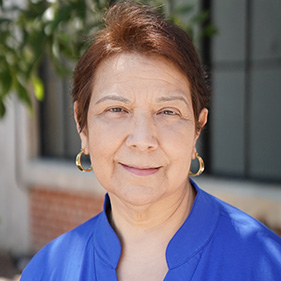 Patient Alma Conteras, wearing a bright blue shirt, smiles outside. 