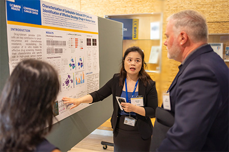 Man with tan jacket and grey hair looking at poster as a woman with dark hair points to her presentation.