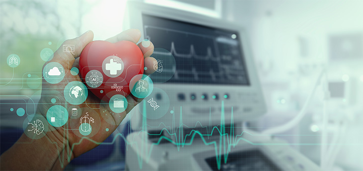 A hand holds a model of a heart in front of medical device’s digital screen