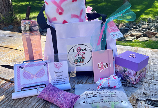 White tote bag with &#x201c;Harvest4Pink&#x201d; logo and an array of items including pillow, cards, box and inspirational sayings.