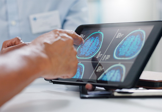 A health care provider points to an image of a brain scan on a computer tablet. 