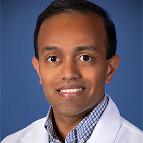 Man with white coat and glasses smiling into camera