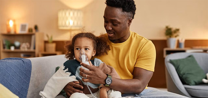 Man holds child with breathing device around nose and mouth.