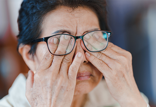 Mujer de mayor edad con cabello corto frotándose con ambas manos los ojos detrás de las gafas