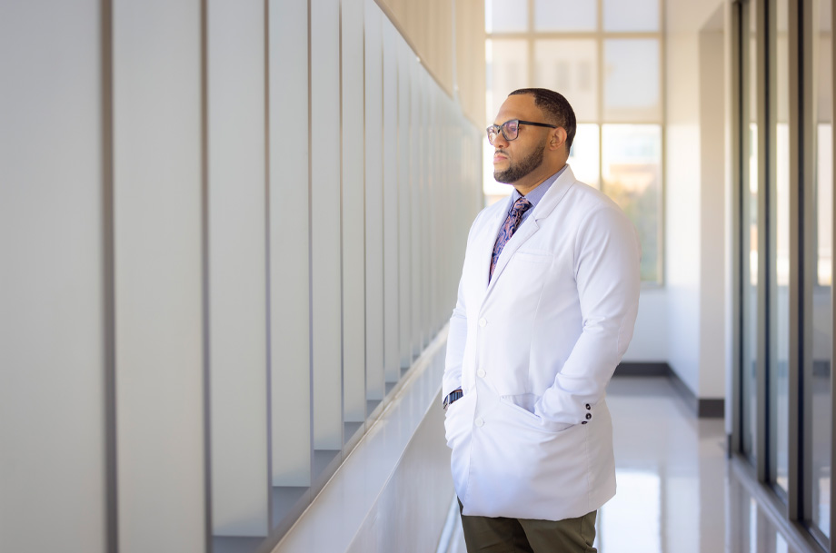 Chris Hall stares with hands in white coat looking out a wall of windows