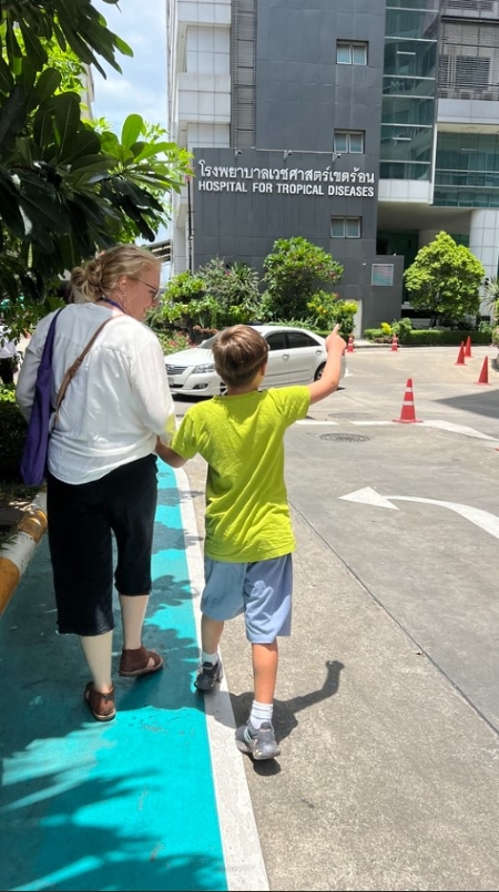 A middle-aged woman holds a young boy’s hand as they cross the street toward a large grey building