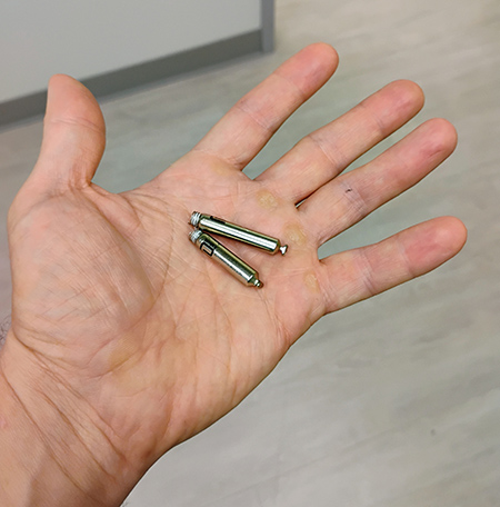 Open hand shows dual chamber leadless pacemaker, made up of two silver cylinders that look like “AA” batteries