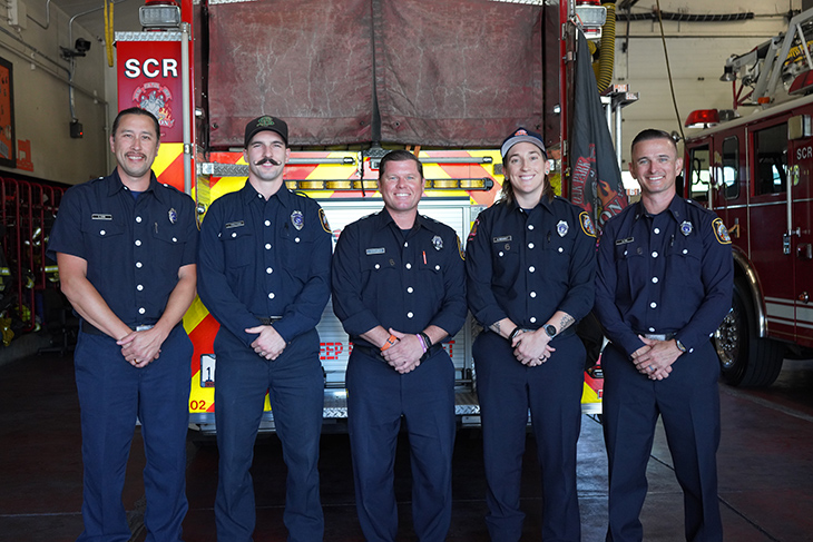 Five firefighters in uniform stand side by side.