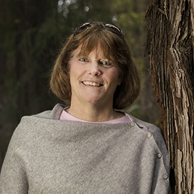 Woman in beige sweater stands next to a redwood tree.