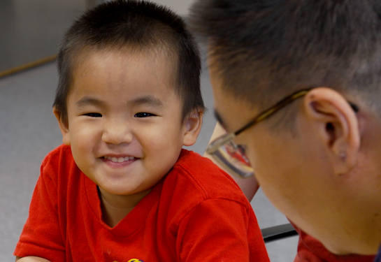 Boy in red shirt smiles at researcher wearing glasses