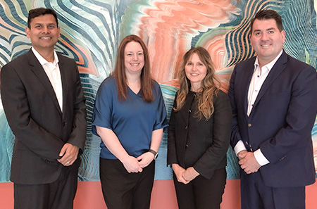 Two men and two women standing side-by-side in front of abstract painting.