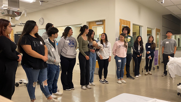 Thirteen high schools students stand in the operating room simulation suite to learn how medical students train with manikins