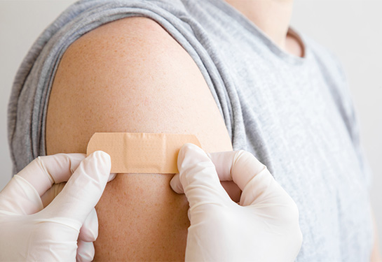 Arm with adhesive bandage placed by someone wearing blue gloves