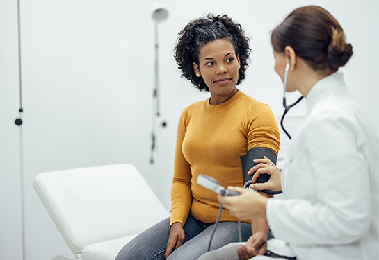 Woman gets her blood pressure checked by a woman wearing a stethoscope and white coat. 