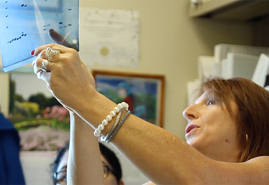 : A female researcher with long red hair holds up a document to the light to examine it