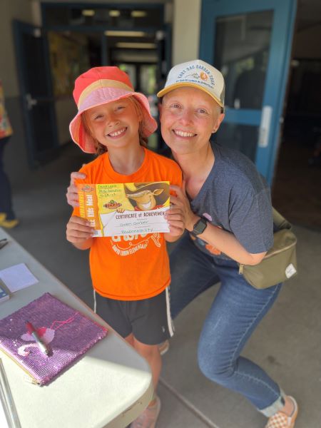 Young girl holding certificate with woman wearing ballcap kneeling beside her.