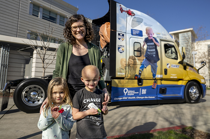 Woman with two children in front of semitruck.