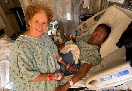 Wee Simla laying in hospital bed and Cynthia McReynolds wearing hospital gown sitting on edge of hospital bed.