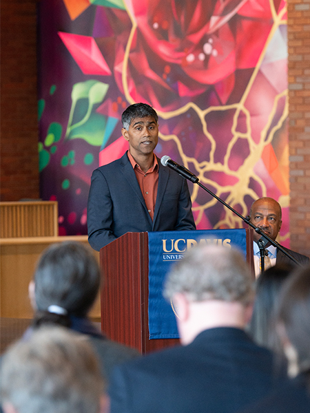 A man stands at the lectern with a mural of a large red rose behind him