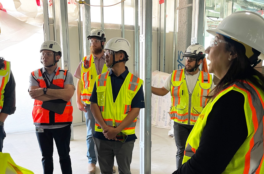 A group of people wearing bright yellow and orange safety vests and hard hats while touring a construction site