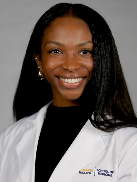 Vertical headshot of a young woman with black hair well past her shoulders smiling, wearing a “School of Medicine” white lab coat