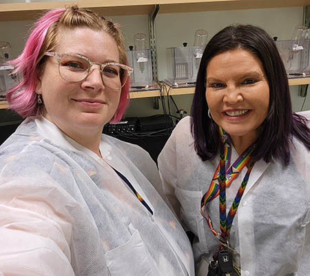 Two researches in protective coats stand together in a lab.