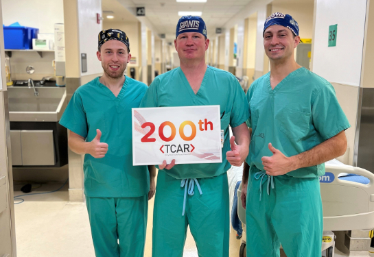 Three people standing together wearing green scrubs holding sign that says 200. 