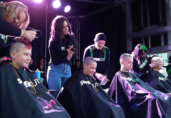 Boys and men getting their hair shaved on stage.