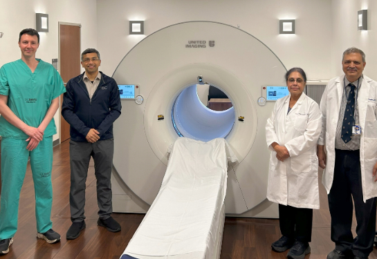 Two people standing on each side machine with narrow bed and donut shaped tube.