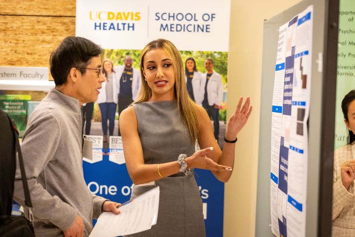 Researcher wearing a grey dress is presenting her poster to a symposium attendee