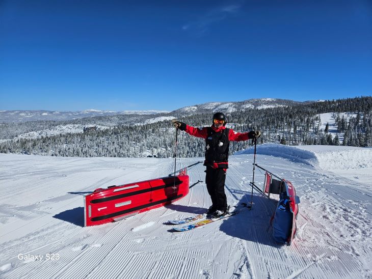 Man in red ski attire raising his hands high with tobaggans in the foreground. 