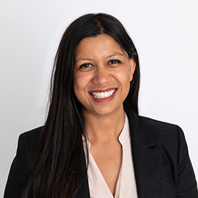 Woman with dark long hair and wearing a dark suit smiling into camera.