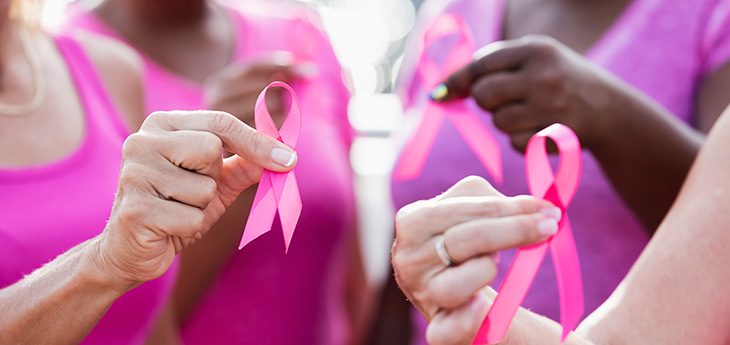 Group of four women with pink shirts holding pink breast cancer ribbons.