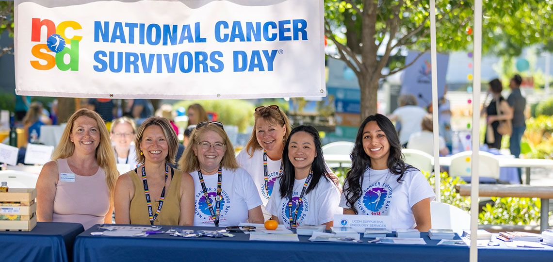 A group of women sitting behind a table with a sign that reads National Cancer Survivors Day