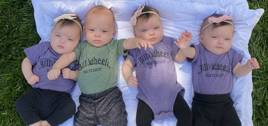 Four babies in matching outfits lying next to one another on a blanket