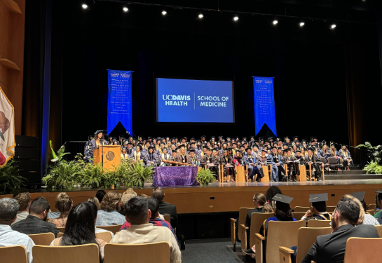Class of 2025 graduates on stage with audience facing them.