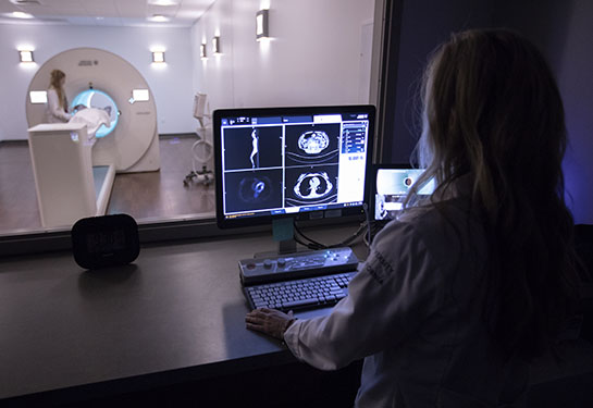 Woman looking at monitor with images in front of room featuring large scanner in background.
