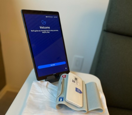 Digital tablet with blue screen and white blood pressure cuff sitting on table.