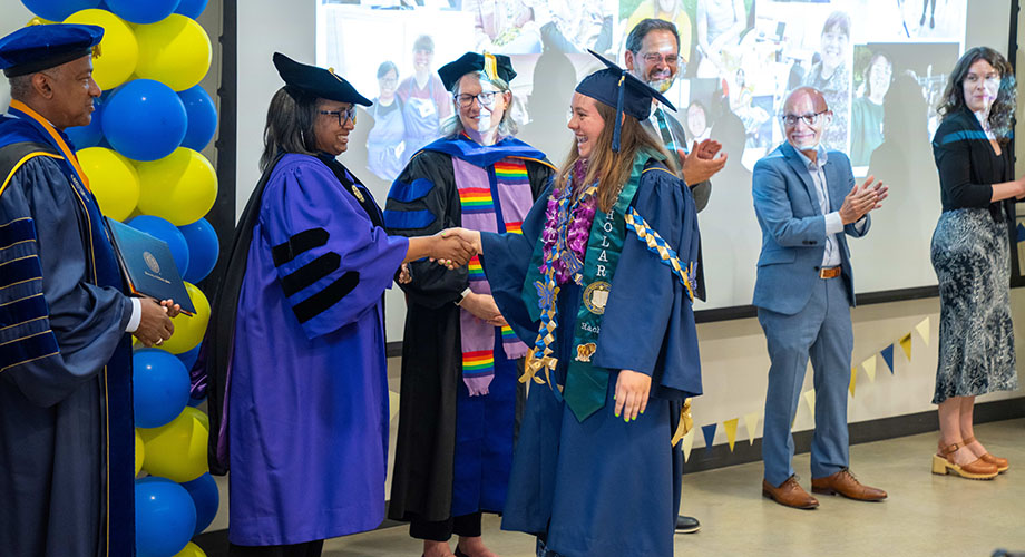 A redwood seed scholar walks across the room shaking hands with a line of people and getting a diploma