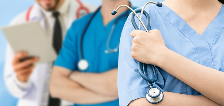 Cropped photo of torsos of three medical professionals with stethoscopes; two are wearing blue scrubs, one has a white lab coat