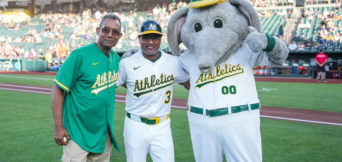 Two men in baseball jerseys standing next to costumed character.