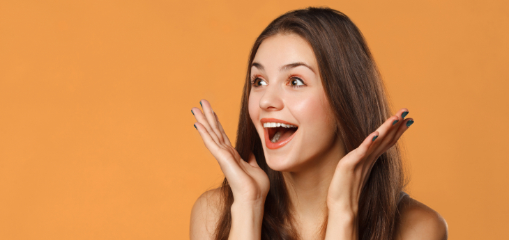Surprised, happy woman with long hair smiles with open hands near her cheeks. 