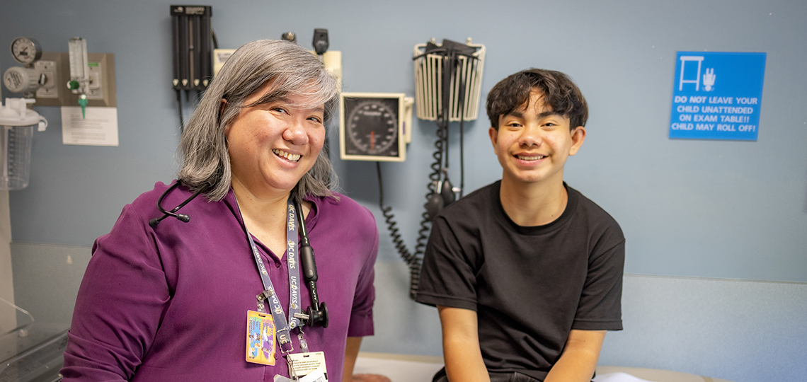 Teen Hispanic boy in black shirt standing next to his Asian female doctor.